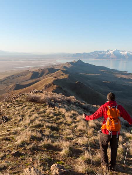 A hiker walking along the ridge of a grassy mountain top.