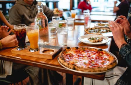 People sitting at a table, sharing and enjoying multiple pizzas.