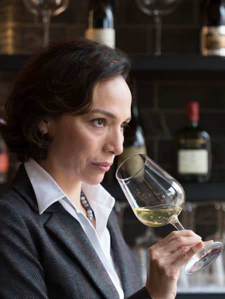 A woman holding a wine glass near her nose, smelling the aroma.