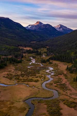 Two mountains with lush green trees framing a spacious valley with a river flowing through it.