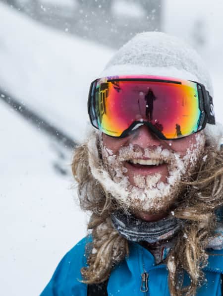 A man smiling while wearing winter clothing, with a long beard covered in snow.