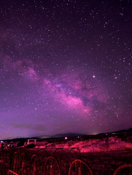 A campground illuminated with a pink hue under a night sky full of bright stars and the Milky Way.