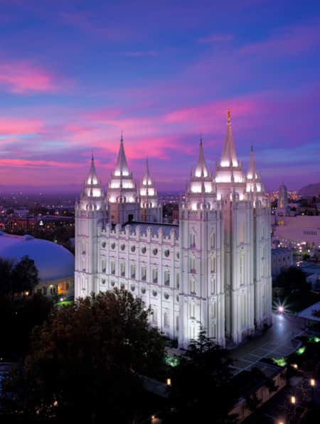 A religious temple illuminated by city lights at sunset, with pink and blue hues in the sky.