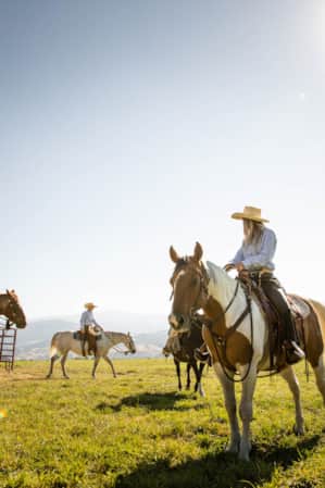 A group of people riding horses in an open field at a ranch.
