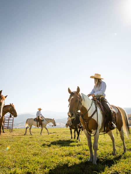 A group of people riding horses in an open field at a ranch.