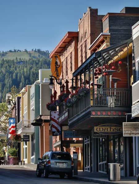 A historic downtown mountain town street, with green mountains and ski runs visible in the distance.