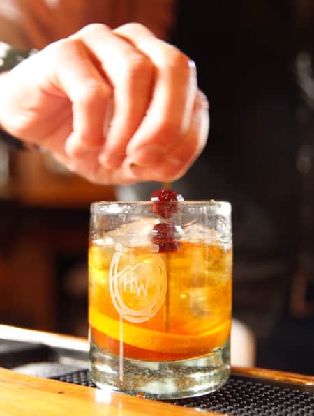 A bartender adding two cherries to the top of a drink.