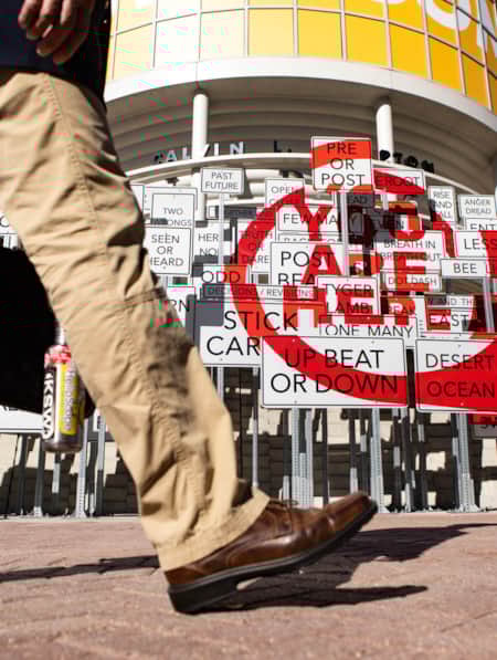 The legs of a person walking past an art installation made of street signs.