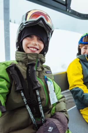 Two young boys wearing winter ski gear inside an enclosed gondola.