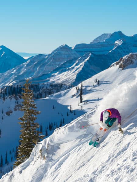 A skier making a turn down a snowy mountain, kicking up a spray of snow behind them.