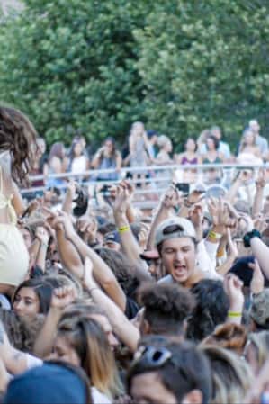 A crowd of people with their hands in the air, singing and facing towards a stage.