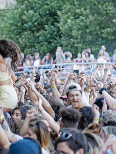 A crowd of people with their hands in the air, singing and facing towards a stage.