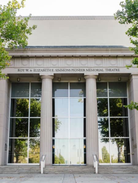 Two tall pillars flanking entrance doors to a building with the name 'Roy W. and Elizabeth E. Simmons Pioneer Memorial Theatre' displayed above.