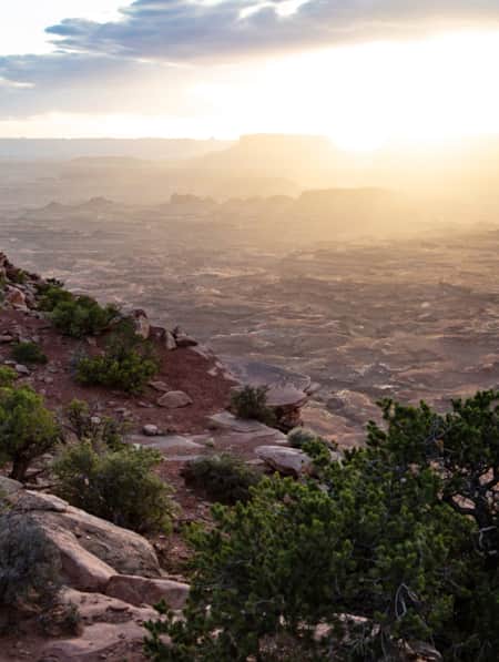 The side of a rocky mountain adjacent to a flat expanse of red rock in the desert.