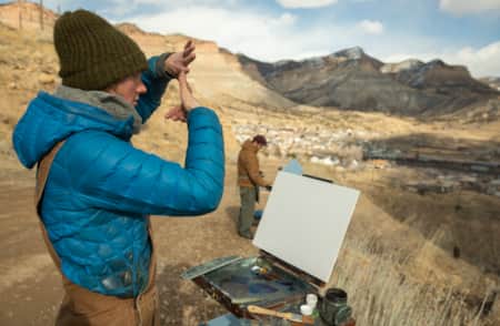 An artist with a canvas in front of them, observing the scenery and preparing to paint.