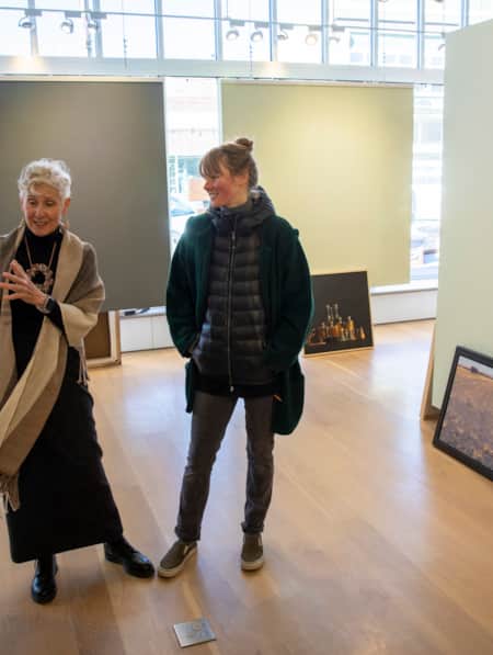 Two women in an art museum, smiling and discussing a piece of artwork.