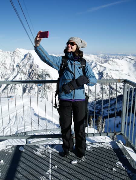 A woman wearing winter gear taking a selfie at the top of a mountain observatory.