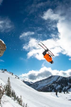 A skier in mid-air, jumping off a rock on a ski run, performing a front flip.