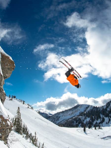 A skier in mid-air, jumping off a rock on a ski run, performing a front flip.