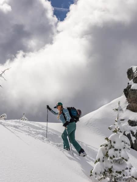 A woman snowshoeing through deep snow on the slope of a mountain.