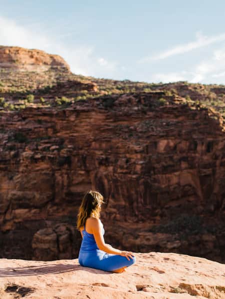 A woman sitting and meditating while overlooking a red rock canyon.
