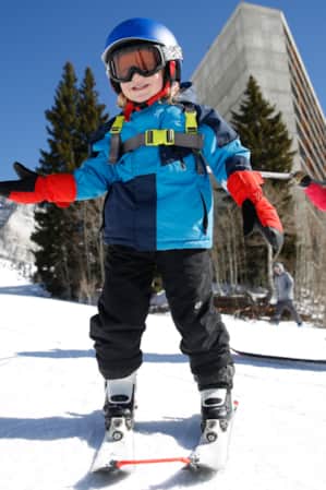 A young child learning how to ski with an adult on a ski run.