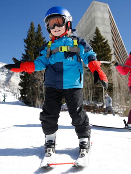 A young child learning how to ski with an adult on a ski run.