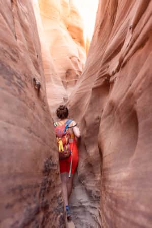 A woman hiking through a narrow slot canyon.