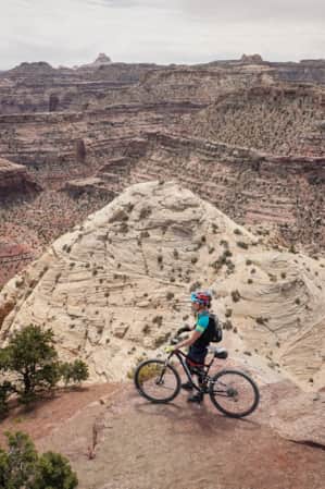 A cyclist at the top of a mountain, overlooking a landscape of large rocky mountains.