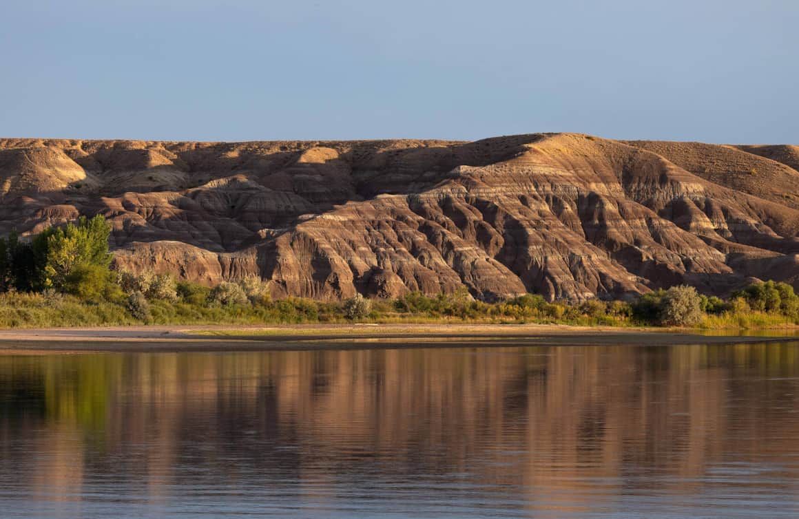 The clay bluffs along the Green River glow before sunset; a great blue heron fishes in the shallows.