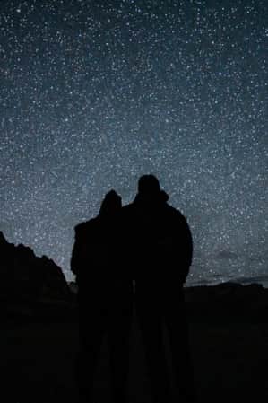 Two people stand in shadow beneath a bright starry sky in Zion National Park.