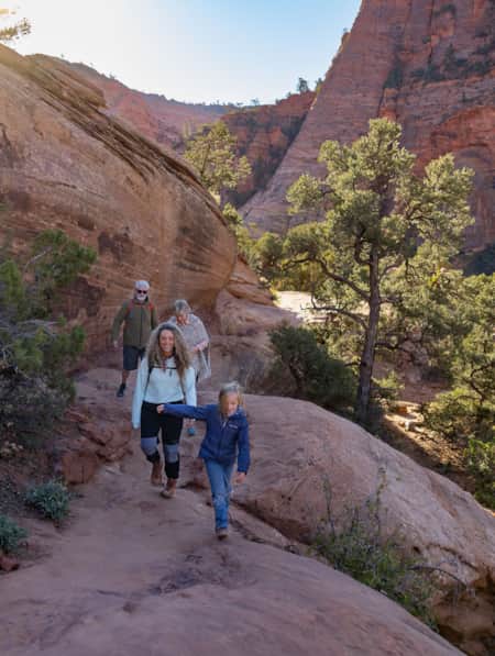 A family hiking in the shade through a red rock landscape.