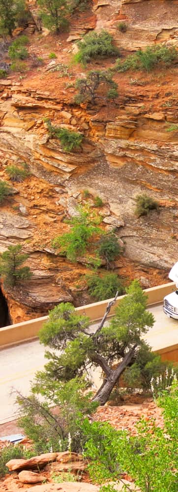 An RV traveling on a road that passes through a red rock tunnel.