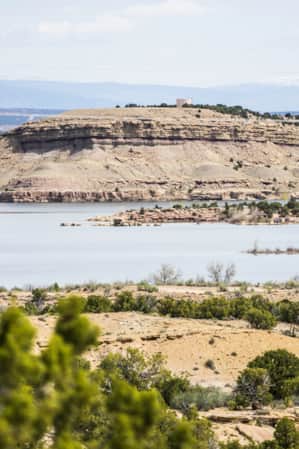 White sandstone rock set upon a hilly landscape, scattered with green bushes, and surrounding a body of water.
