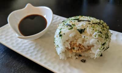 A half-eaten rice ball on a plate with sauce.
