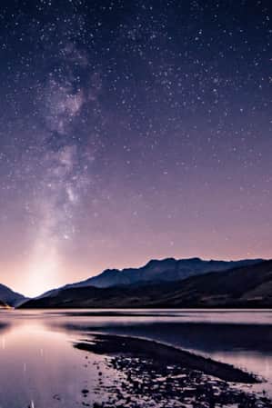 A night sky full of stars reflecting onto a lake.