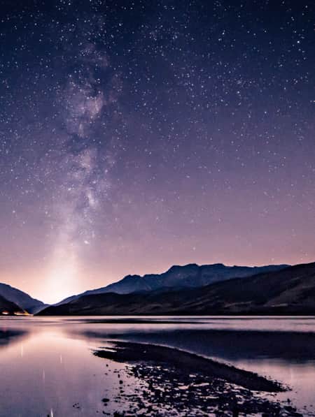 A night sky full of stars reflecting onto a lake.