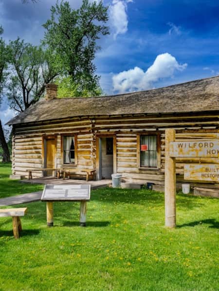 An old home made of wood logs, with a sign in the front yard reading 'Wilford Woodruff Home.'