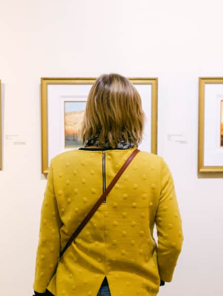 View of a woman from behind, observing three art pieces hanging on a wall.