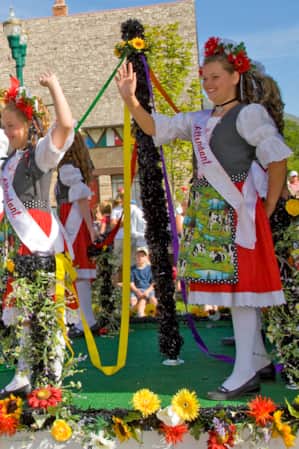 oung girls on a parade boat waving to bystanders, dressed in traditional German attire.