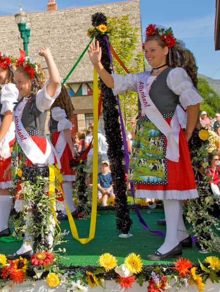 oung girls on a parade boat waving to bystanders, dressed in traditional German attire.