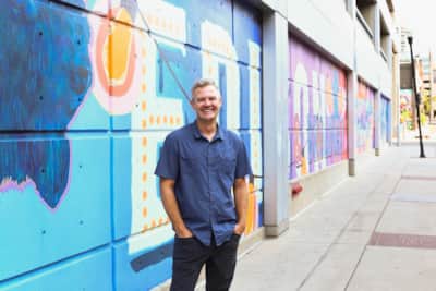 Mural artist Chris Peterson stands alongside one of his creations.