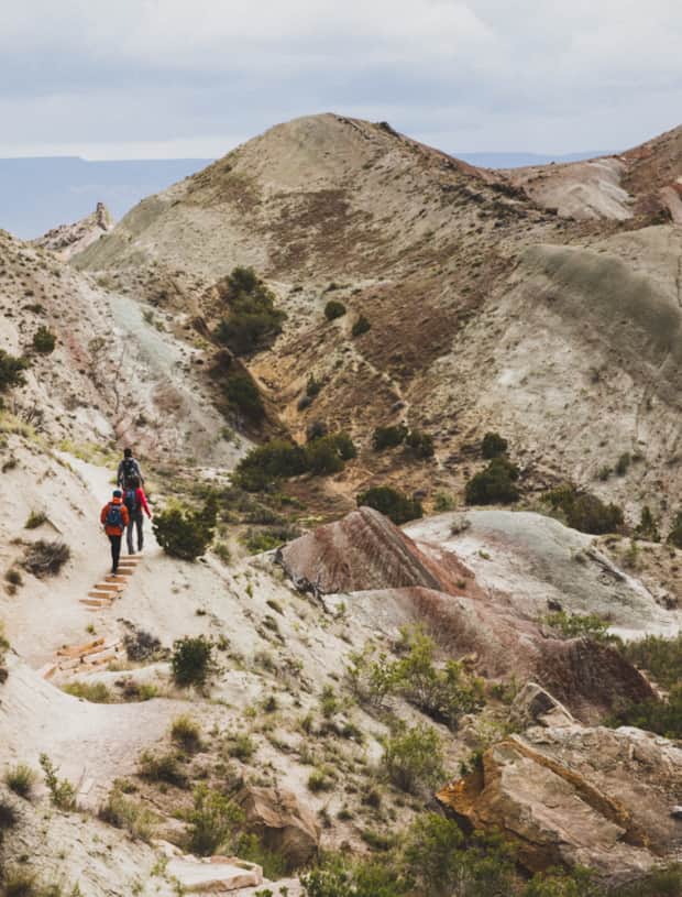 Hikers walking along a sandy trail among the hills of Dinosaur National Monument.
