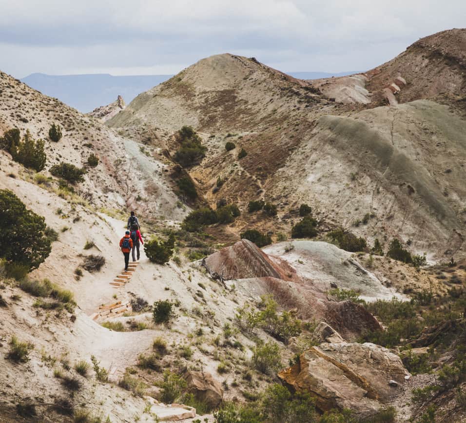 Hikers walking along a sandy trail among the hills of Dinosaur National Monument.