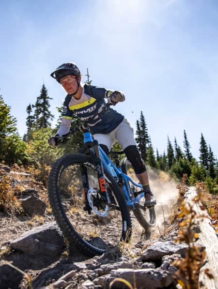 A woman riding a mountain bike down a rocky dirt trail, leaving a trail of dust behind her.
