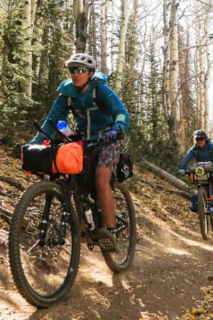 Three people riding mountain bikes in a line, coming down a trail surrounded by trees.