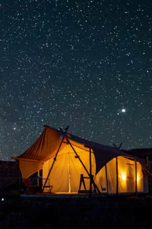 A canvas tent illuminated by a porch light under a starry sky with the Milky Way visible.