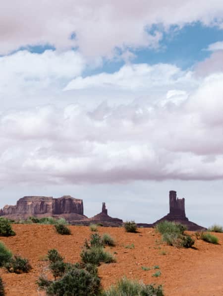 Two people hiking on a cloudy day along a path leading towards large monuments in the distance.