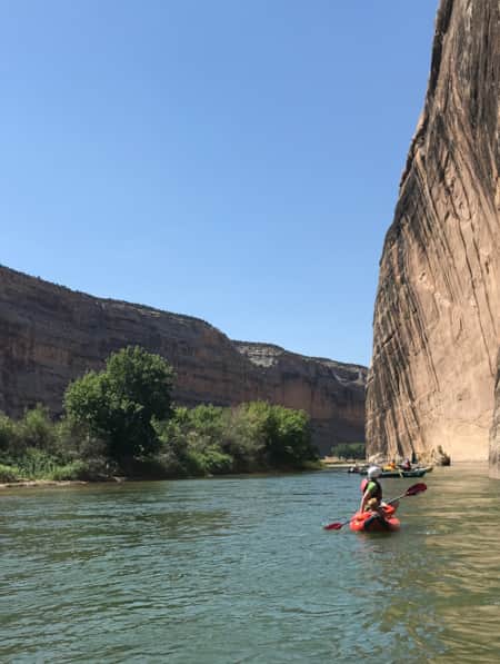 People rafting on the water, navigating between large cliffs.