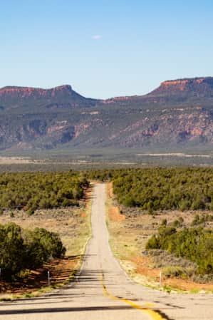 narrow road leading toward two mountains with flat tops.